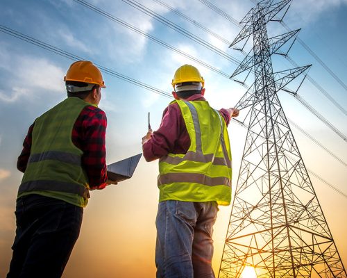 Picture of two electrical engineers using a notebook computer standing at a power station to view the planning work by producing electrical energy at high voltage electrodes.